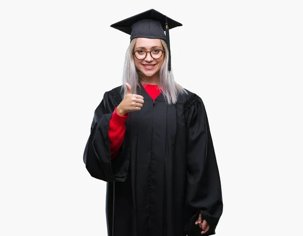 若いブロンドの女性は 幸せな親指の手でジェスチャーを行う分離の背景に大学院の制服を着ています 成功を示すと カメラを見て式を承認します — ストック写真