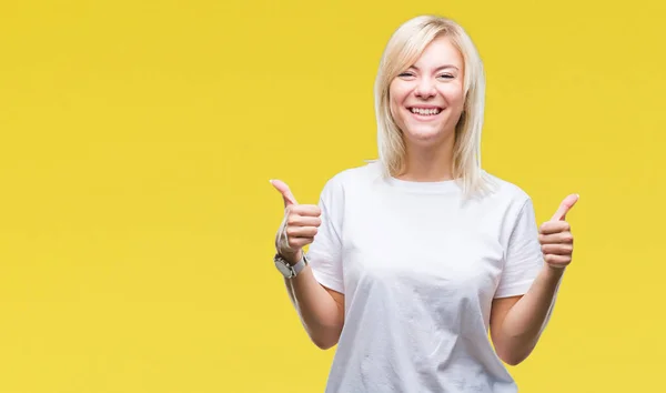 年轻美丽的金发女子穿白色 T恤在孤立的背景成功标志做积极的手势与手 竖起大拇指微笑和快乐 用欢快的表情看着相机 胜利者的手势 — 图库照片