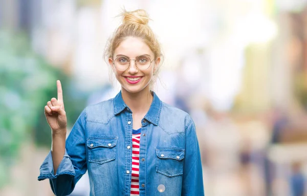 年轻美丽的金发女子戴着眼镜在孤立的背景显示和指向与手指第一 而微笑自信和快乐 — 图库照片