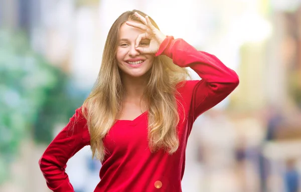 幸せそうな顔で指を通して見る目の手で のジェスチャーを行う分離の背景に赤いセーターを着ている若い美しいブロンドの女性 — ストック写真