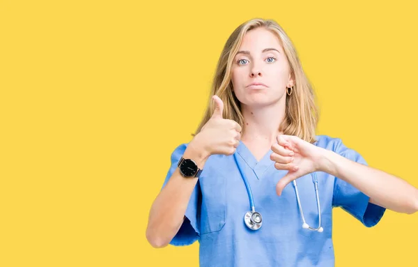 美丽的年轻医生妇女穿着医疗制服在孤立的背景做大拇指向上和向下 分歧和协议表达 疯狂的冲突 — 图库照片