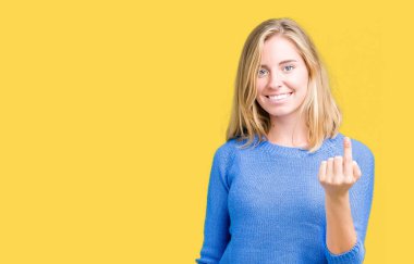 Beckoning gel burada mutlu ve gülümseyerek el davet ile jest izole arka plan üzerinde mavi kazak giyen güzel genç kadın