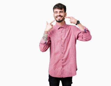 Kendinden emin gösterilen ve işaret parmakları diş ve ağız ile gülümseyen izole arka plan üzerinde pembe gömlek giymiş yakışıklı delikanlı. Sağlık kavramı.