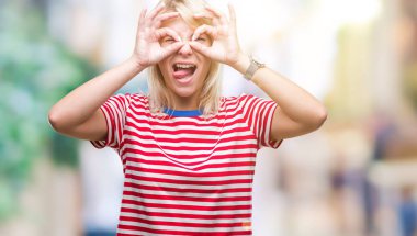 Genç güzel sarışın kadın dilini, parmaklarının arasından baktığını yapışmasını dürbün gibi ok jest yapıyor izole arka plan yüzünden. Deli ifade.