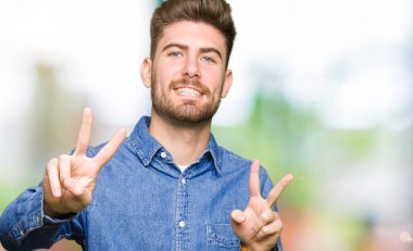 Genç yakışıklı sarışın adam giyiyor rahat denim gömlek zafer işareti yapıyor parmak gösterilen kamera seyir gülümseyen. İki numaralı.