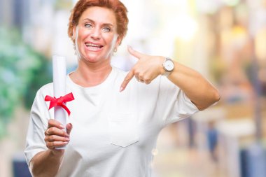 Sürpriz yüz işaret parmağı kendini izole arka plan üzerinde derece sertifika tutan kıdemli beyaz kadın