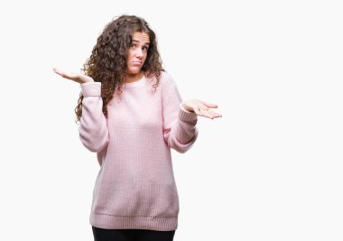 Güzel esmer kıvırcık saçlı Genç kız üzerinde pembe kış kazak giyiyor arka plan clueless ve şaşkın bir ifadeyle kollar ve eller kaldırdı izole. Şüphe kavramı.