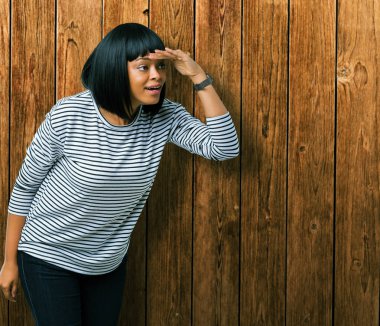 Üzerinde çizgili süveter giyen güzel genç Afro-Amerikan kadın arka plan çok mutlu ve gülümseyen uzakta el ile üzerine kafa seyir izole. Arama kavramı.