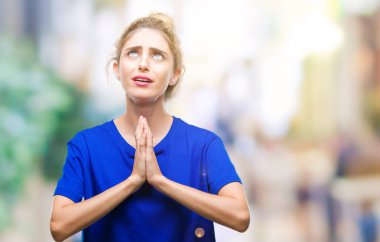 Yalvarıyor ve umut ifade yüzünde çok duygusal ve endişe ile birlikte elleriyle dua izole arka plan üzerinde mavi t-shirt giyen genç güzel sarışın ve mavi gözlü kadın. Bağışlanmak. Din kavramı.