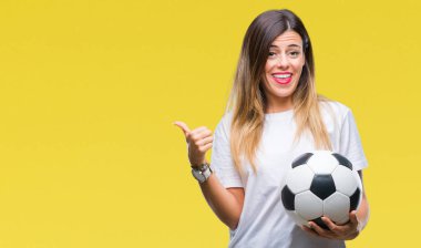 İşaret ve başparmak kadar mutlu yüz gülümseyen tarafı ile gösteren izole arka plan üzerinde futbol topu tutan genç güzel kadın