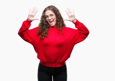 Gösterilen ve parmakları ile işaret izole arka plan üzerinde gözlük ve kış kazak giyen güzel esmer kıvırcık saçlı Genç kız kendinden emin ve mutlu gülümseyerek süre on numara.