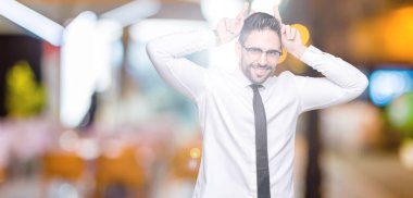 Komik ve çılgın baş parmaklar ile kulakları, tavşan poz izole arka plan üzerinde gözlüklü genç yakışıklı iş adamı neşeli gülümseyen