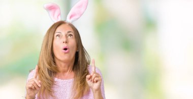 Paskalya tavşan kulakları izole arka plan üzerinde giyen orta yaş esmer kadın hayrete ve yukarıya bakıyor ve parmakları ile işaret ve silah kaldırdı şaşırttı.