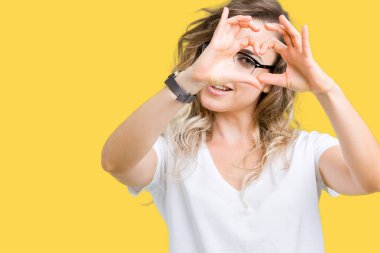 İzole arka plan yaparken kalp şekli el ve parmak işareti seyir gülümseyen ile üzerinde gözlük güzel sarışın genç kadın