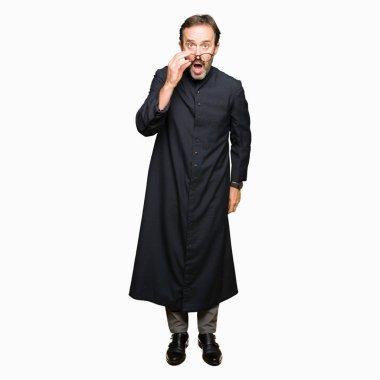 Orta yaş rahip adam korkuyor ve şok sürpriz ifade, korku ve heyecan yüz ile Katolik bornoz giymiş.