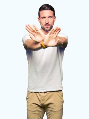 Yakışıklı adam rahat beyaz t-shirt giyen ret ifade geçiş silah ve avuç içi eksi işareti, kızgın surat yapıyor