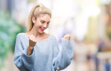 Gülümseyen ve başarı için çığlık izole arka plan çok mutlu ve heyecanlı kaldırdı, silah ile kazanan jest yapıyor üzerinde kış kazak giyen genç güzel sarışın ve mavi gözlü kadın. Kutlama kavramı.