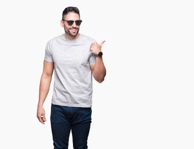 Yakışıklı delikanlı işaret ve başparmak kadar mutlu yüz gülümseyen tarafı ile gösteren izole arka plan üzerinde güneş gözlüğü takıyor