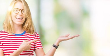 Güzel genç kadın hayrete ve el ile sunulması ve parmak ile işaret ederken kameraya gülümseyen izole arka plan üzerinde gözlük.