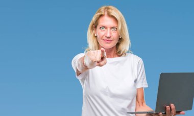 Kamera ve size parmak ile işaret arka plan üzerinde bilgisayar dizüstü kullanan orta yaş sarışın kadın izole, el işareti, pozitif ve kendinden emin bir jest ön