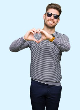 Genç yakışıklı adam aşık kalp simgesi ve elleriyle şekil gösteren gülümseyen güneş gözlüğü takıyor. Romantik kavramı.