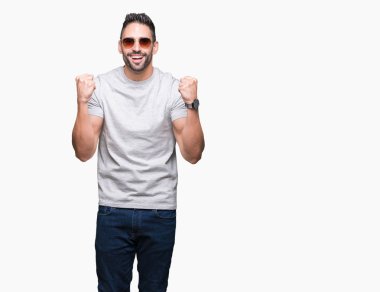 Yakışıklı delikanlı izole arka plan kutlama üzerinde güneş gözlüğü takıyor şaşırttı ve başarı için kaldırdı kollarını açarak hayret ve gözleri açık. Kazanan kavramı.