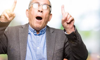 Gözlük takan yakışıklı üst düzey businesss adam hayret ve yukarıya bakıp parmakları ile işaret şaşırttı ve silah kaldırdı.