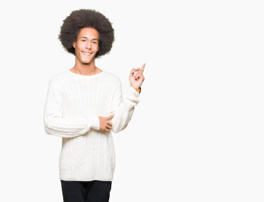 Yüzünde, kocaman bir gülümseme ile kış kazak giyen afro saçlı genç Afro-Amerikan adam kameraya bakarak yan el ve parmak ile işaret.