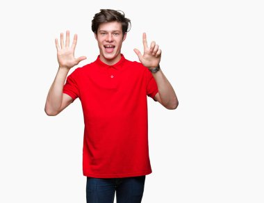 Gösterilen ve parmakları ile işaret izole arka plan üzerinde kırmızı t-shirt giyen genç yakışıklı adam kendinden emin ve mutlu gülümseyerek süre yedi numara.