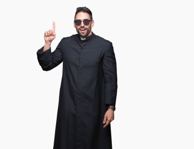 Genç Hıristiyan rahip giyen güneş gözlüğü izole arka plan üzerinde işaret parmağı kadar başarılı fikir. Çıktıktan ve mutlu. Bir numara.
