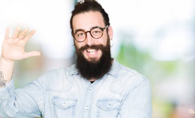 Uzun saç ve sakal ile büyük ve büyük boy işaret, ölçü birimi sembol gösteren el eller gözlüklü genç hipster adam. Kameraya bakarak gülümsüyordu. Ölçüm kavramı.