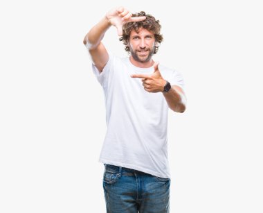 Yakışıklı İspanyol modeli adam elleriyle yapım çerçeve ve parmakları ile mutlu yüz gülümseyen izole arka plan üzerinde. Yaratıcılık ve Fotoğrafçılık kavramı.
