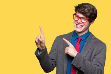 Gülümseyen ve iki elleri ve parmakları ile tarafına işaret kamera bakarak izole arka plan üzerinde kırmızı gözlük takan genç yakışıklı iş adamı.