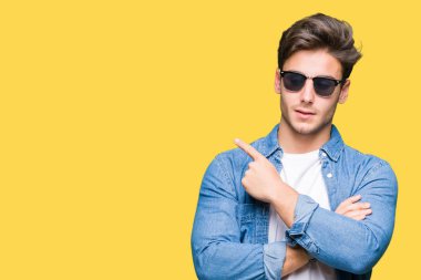 Genç yakışıklı adam giyen güneş gözlüğü izole üzerinde işaretleme için reklam, ciddi ve sakin yüz gösterilen yan el parmak ile arka plan