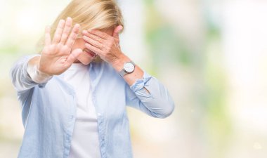 Orta yaş sarışın kadın izole elleriyle gözlerini kapsayan arka plan ve stop jest ile acı ve korku ifadesi. Utandım ve negatif kavramı.