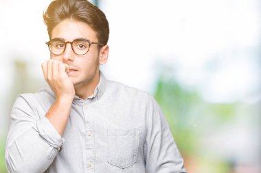 Genç yakışıklı adam stresli ve gergin ile izole arka plan üzerinde gözlük takan tırnak ısırma dudaklarından eller. Anksiyete sorunu.