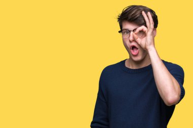 Sürpriz yüz, göz parmaklarının arasından seyir ile ok jest yapıyor izole arka plan üzerinde gözlüklü genç yakışıklı adam şok. İmansız ifade.