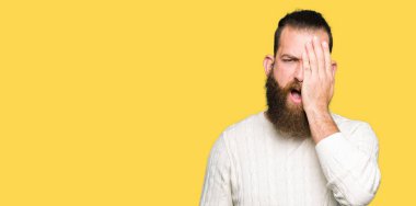 Kış kazak yarım yüz, göz ve ağız el ile kapsayan yorgun esneme giyen genç hipster adam. Acı yüzü acıyor.