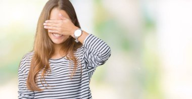 Gülümsüyor ve gözleri için sürpriz kapsayan yüz el ile gülüyor izole arka plan üzerinde çizgili süveter giyen genç güzel esmer kadın. Kör kavramı.