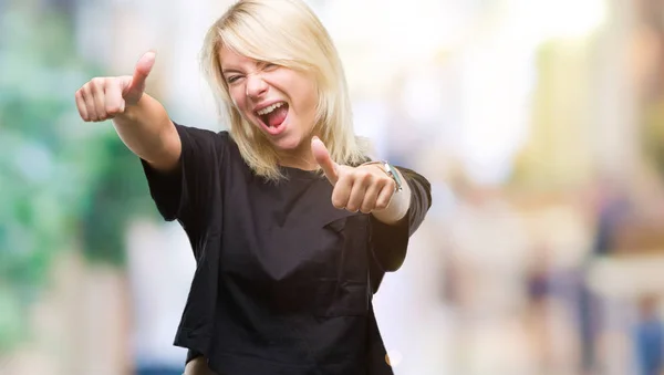 Young beautiful blonde woman over isolated background approving doing positive gesture with hand, thumbs up smiling and happy for success. Looking at the camera, winner gesture.