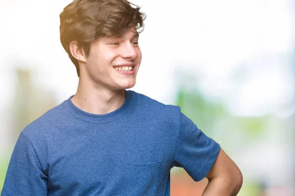 年轻的帅哥穿着蓝色的 T恤在孤立的背景看着一边 面带微笑 自然的表情 笑自信 — 图库照片