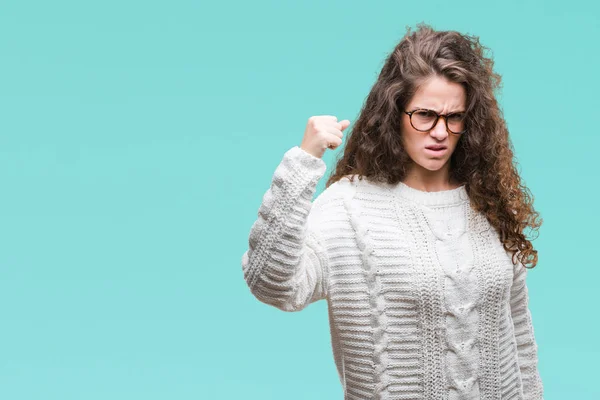 Beautiful brunette curly hair young girl wearing winter sweater over isolated background angry and mad raising fist frustrated and furious while shouting with anger. Rage and aggressive concept.