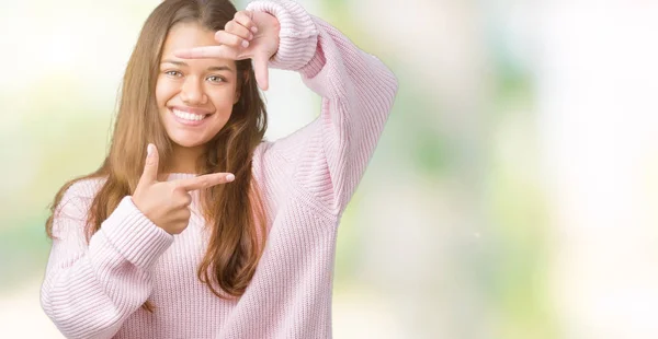 笑顔の幸せそうな顔で指と手作りフレーム分離の背景の上ピンク冬のセーターを着た若い美しいブルネット女性 創造性と写真のコンセプト — ストック写真