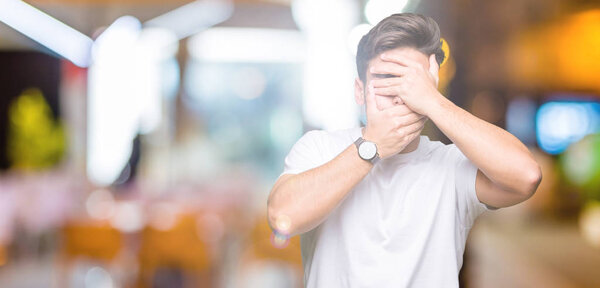 Young handsome man wearing white t-shirt over isolated background Covering eyes and mouth with hands, surprised and shocked. Hiding emotion