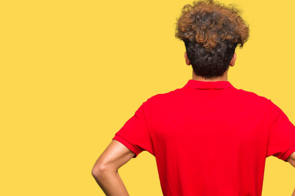 Молодой красивый мужчина с афроволосами в красной футболке, стоящий задом наперёд и смотрящий с руками на тело.

