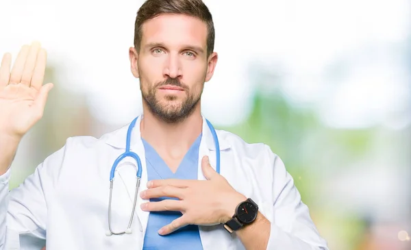 Handsome doctor man wearing medical uniform over isolated background Swearing with hand on chest and open palm, making a loyalty promise oath