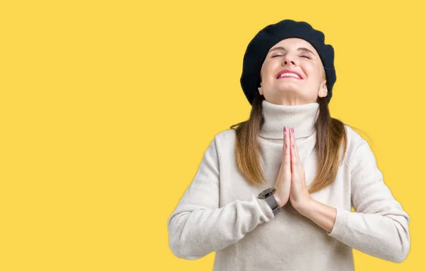 Middle age mature woman wearing winter sweater and beret over isolated background begging and praying with hands together with hope expression on face very emotional and worried. Asking for forgiveness. Religion concept.