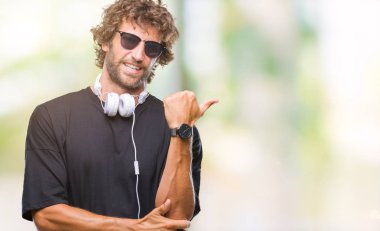 İspanyol yakışıklı seyir ve başparmak yanında yukarıyı mutlu yüz ile gülümseyen izole arka plan üzerinde kulaklık giyen müzik dinlemek.