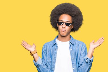 Afrikalı-Amerikalı genç afro saçlı thug hayat gözlük clueless ve şaşkın ifade kollar ve eller kaldırdı ile giyiyor. Şüphe kavramı.