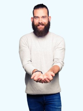 Casual kazak el avuç içi ile birlikte gülümseyen giyen genç sarışın adam alma veya jest vererek. Ayrı tutma ve koruma